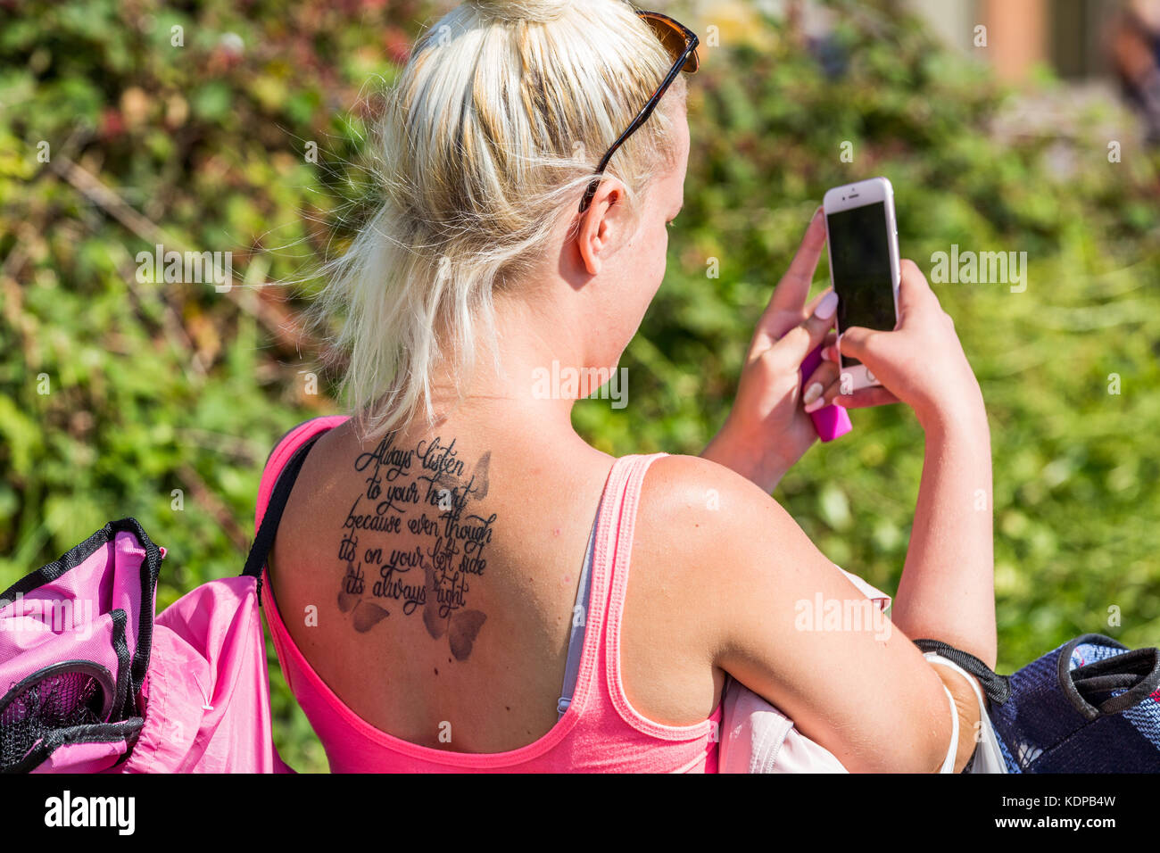 A young blonde hair woman wearing a low cut top and sunglasses with a tattoo on her back taking a selfie photo, Bournemouth, England UK Stock Photo