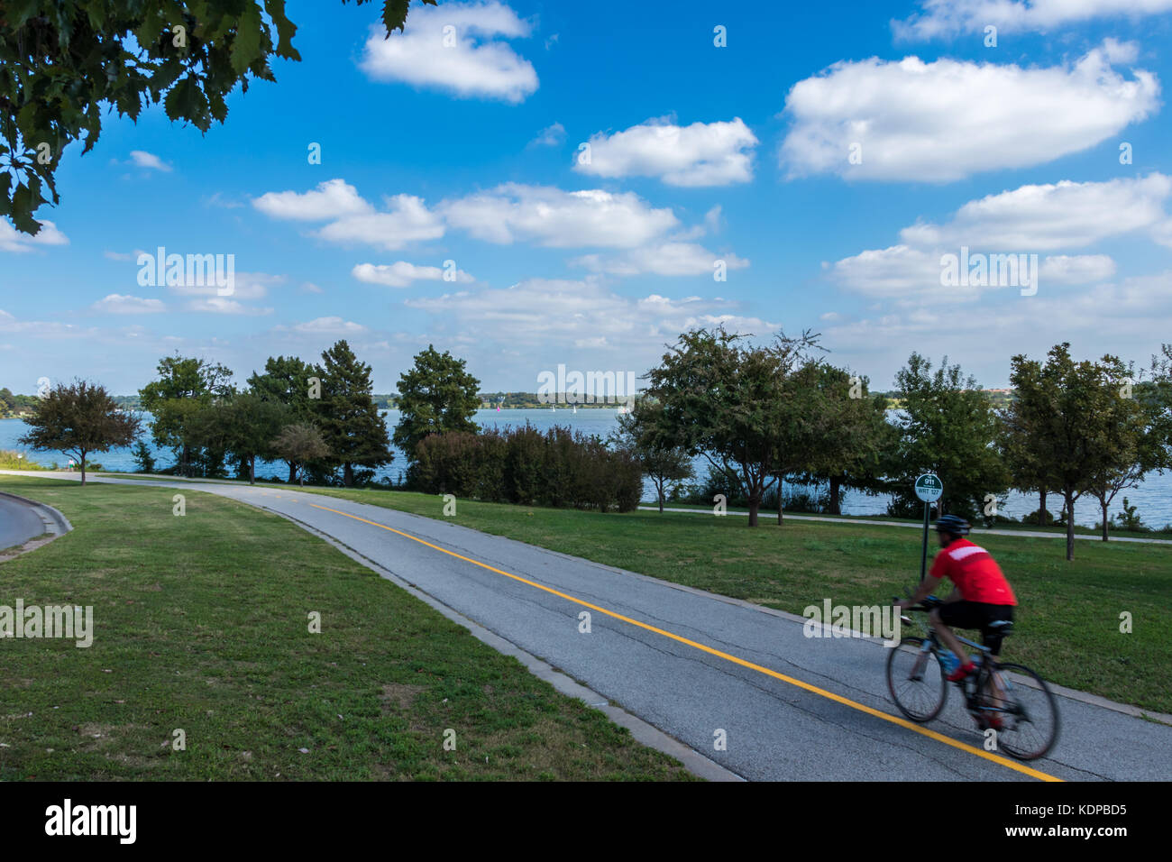 Lone male cyclist on  a bike trail with lake and sailboats in background speeding by Stock Photo
