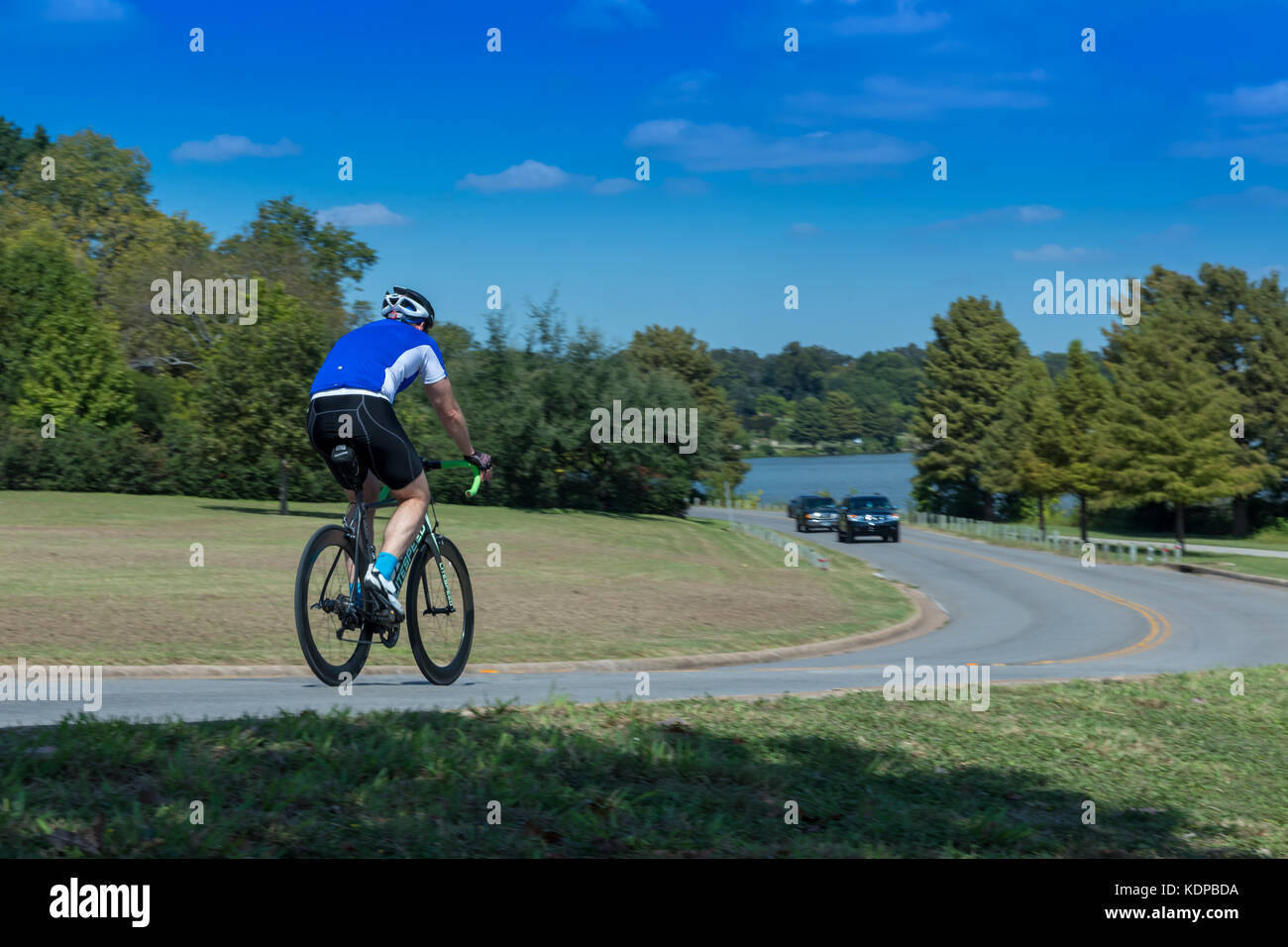 Lone male cyclist on  a bike trail with lake in bacground heading away Stock Photo