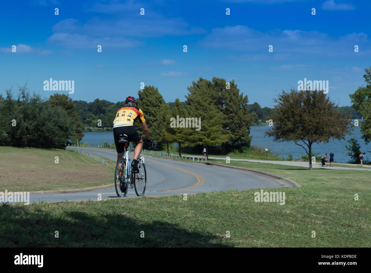 Lone male cyclist on  a bike trail with lake in background heading away Stock Photo