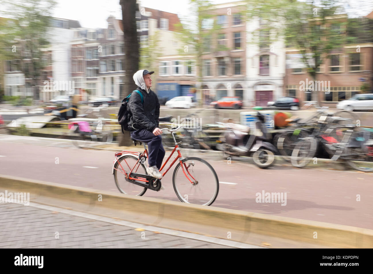 a young casually dressed man cycles through central Amsterdam Stock Photo
