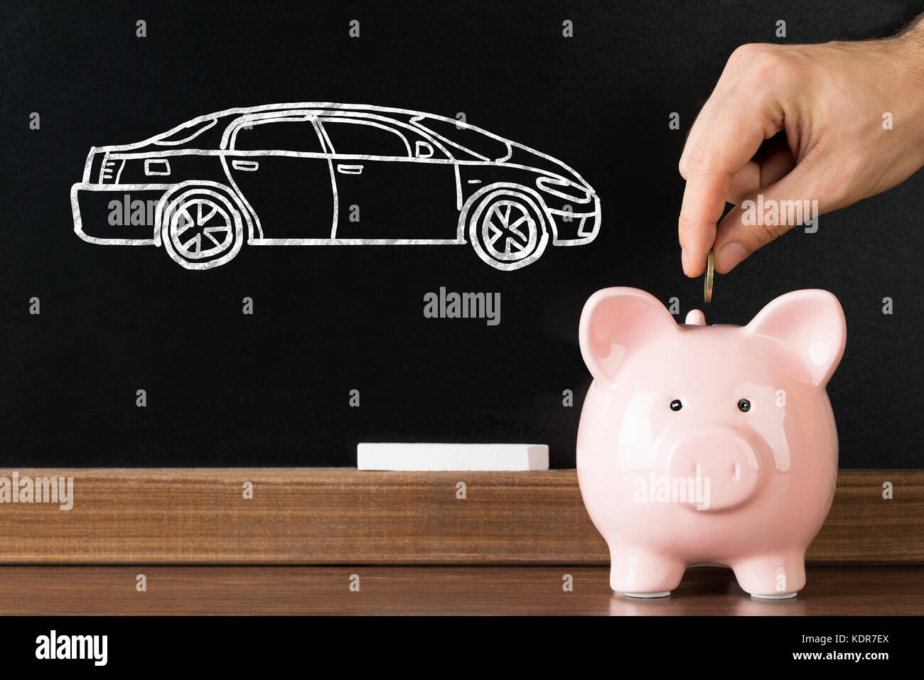 Person Hand Inserting Coin In Piggybank With Car Image Drawn On Blackboard At Background Stock Photo