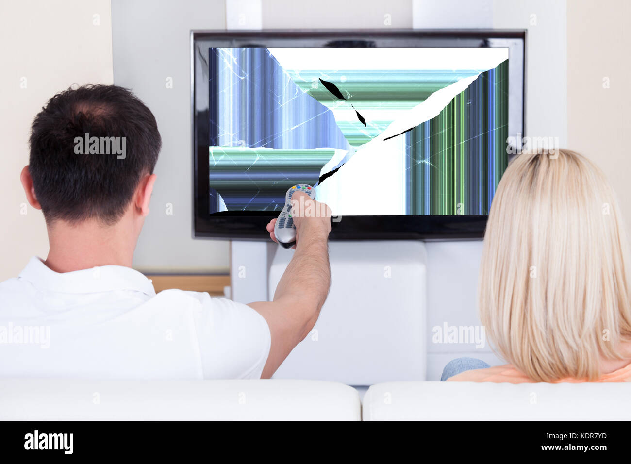Couple With Remote Control In Front Of Television Showing Distorted Screen At Home Stock Photo