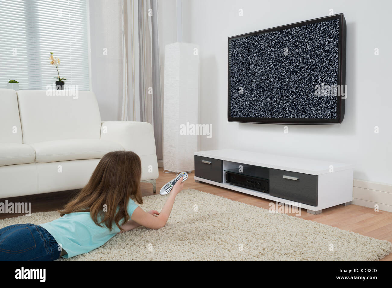 Girl With Remote Control Lying On Carpet In Front Of Television With No Signal Stock Photo