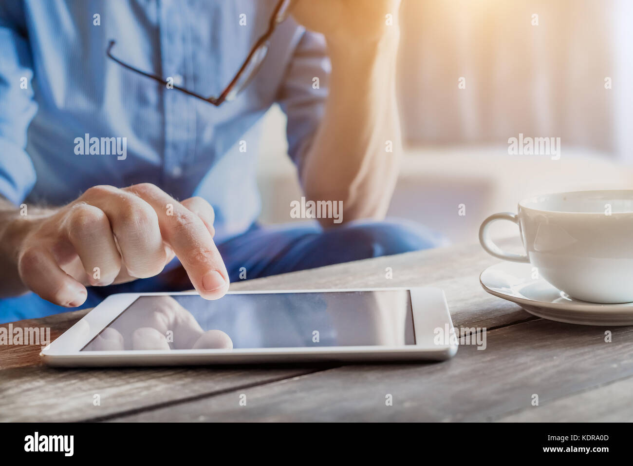 Young businessman using digital tablet computer on a wooden table with a cup of coffee, male hand touching screen, blurred background Stock Photo