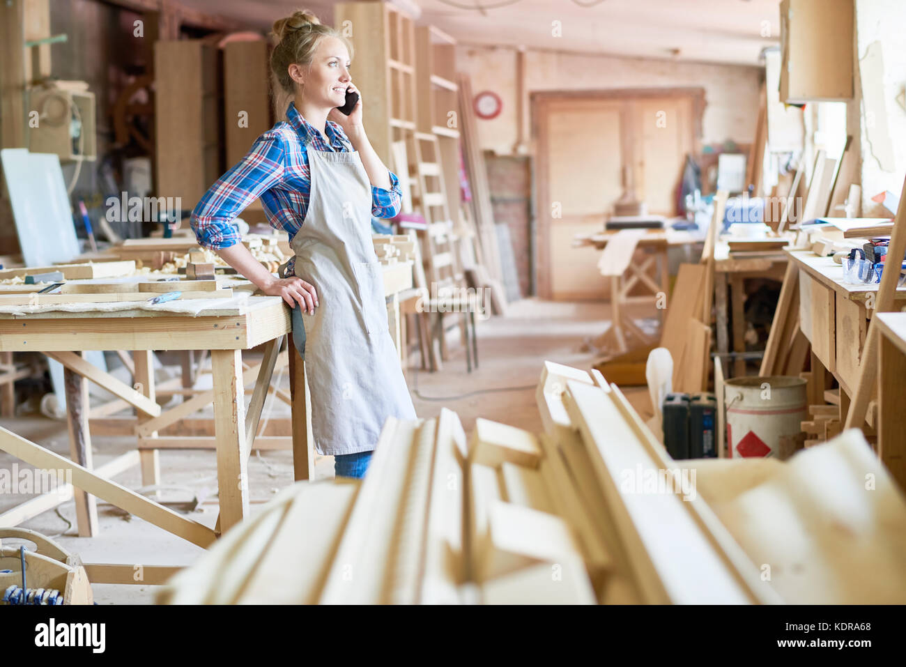 Female Carpenter Speaking By Smartphone in Modern Workshop Stock Photo