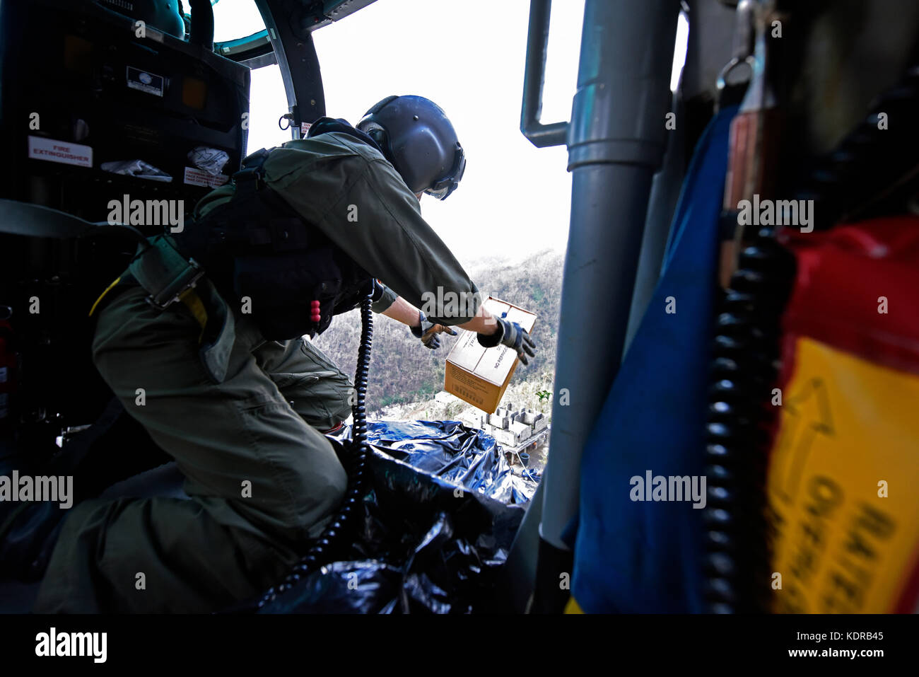 A U.S. Coast Guard officer drops emergency supplies out of a MH-65 Dolphin helicopter to Puerto Rican residents below during relief efforts in the aftermath of Hurricane Maria October 3, 2017 near Utuado, Puerto Rico. The residents were stranded after the hurricane caused mudslides and washed out roads. Stock Photo