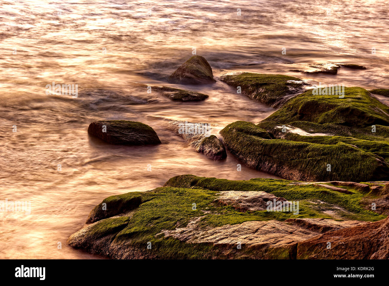 Sea water dripping between rocks during summer sunset Stock Photo