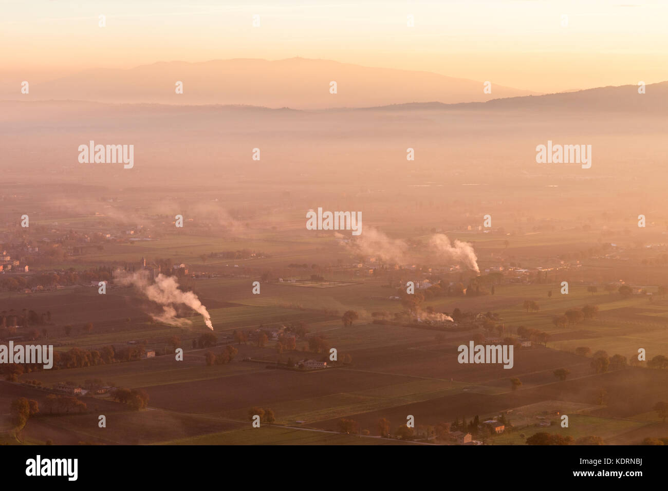 A valley in Umbria at sunset, with some smoke and mist, distant hills and beautiful warm, orange tones Stock Photo