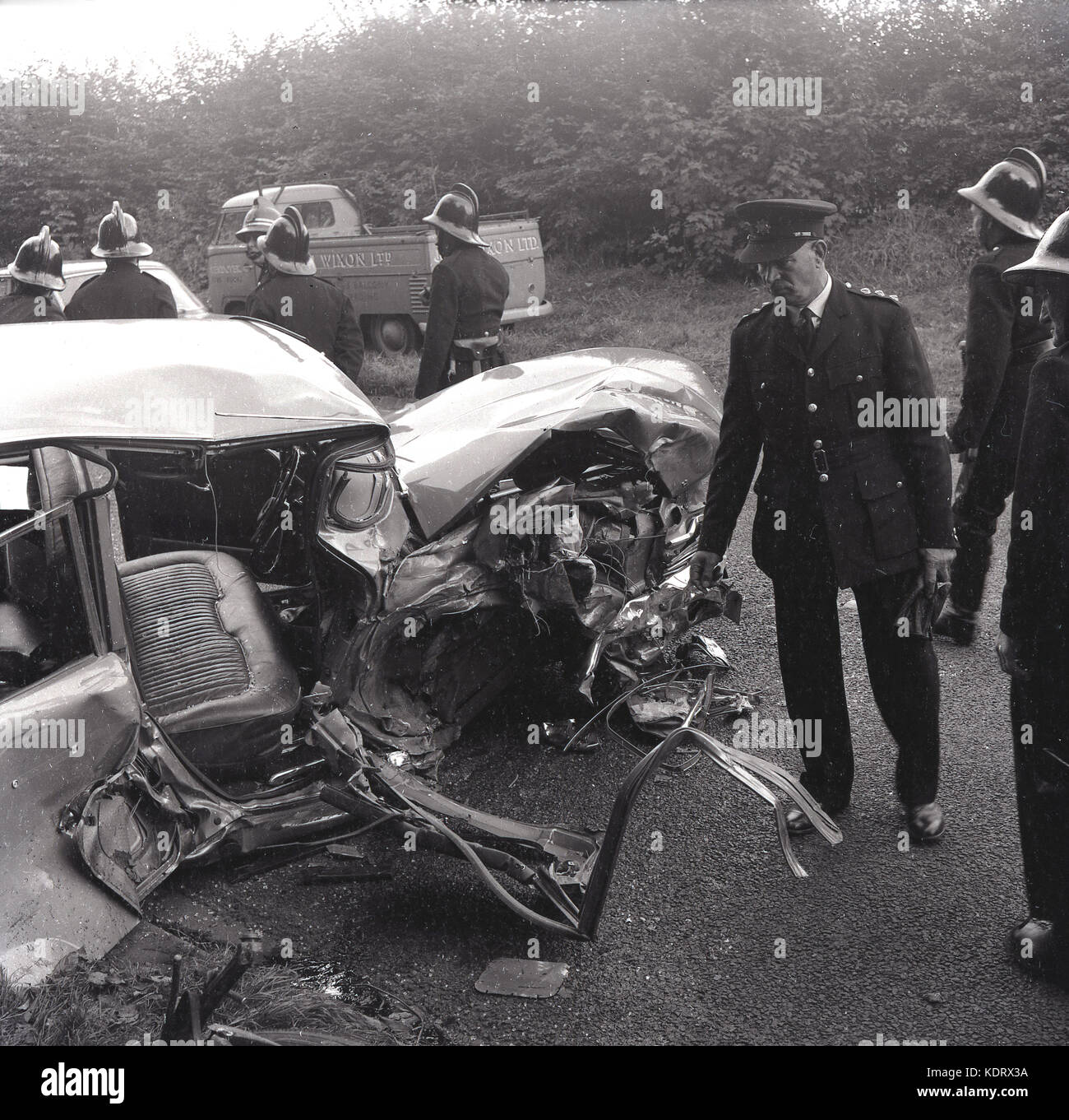 1960s, Buckinghamshire, UK, poiice and firemen with helmets at the scene of a rural road accident and a severely smashed up motorcar lying on the road. Stock Photo