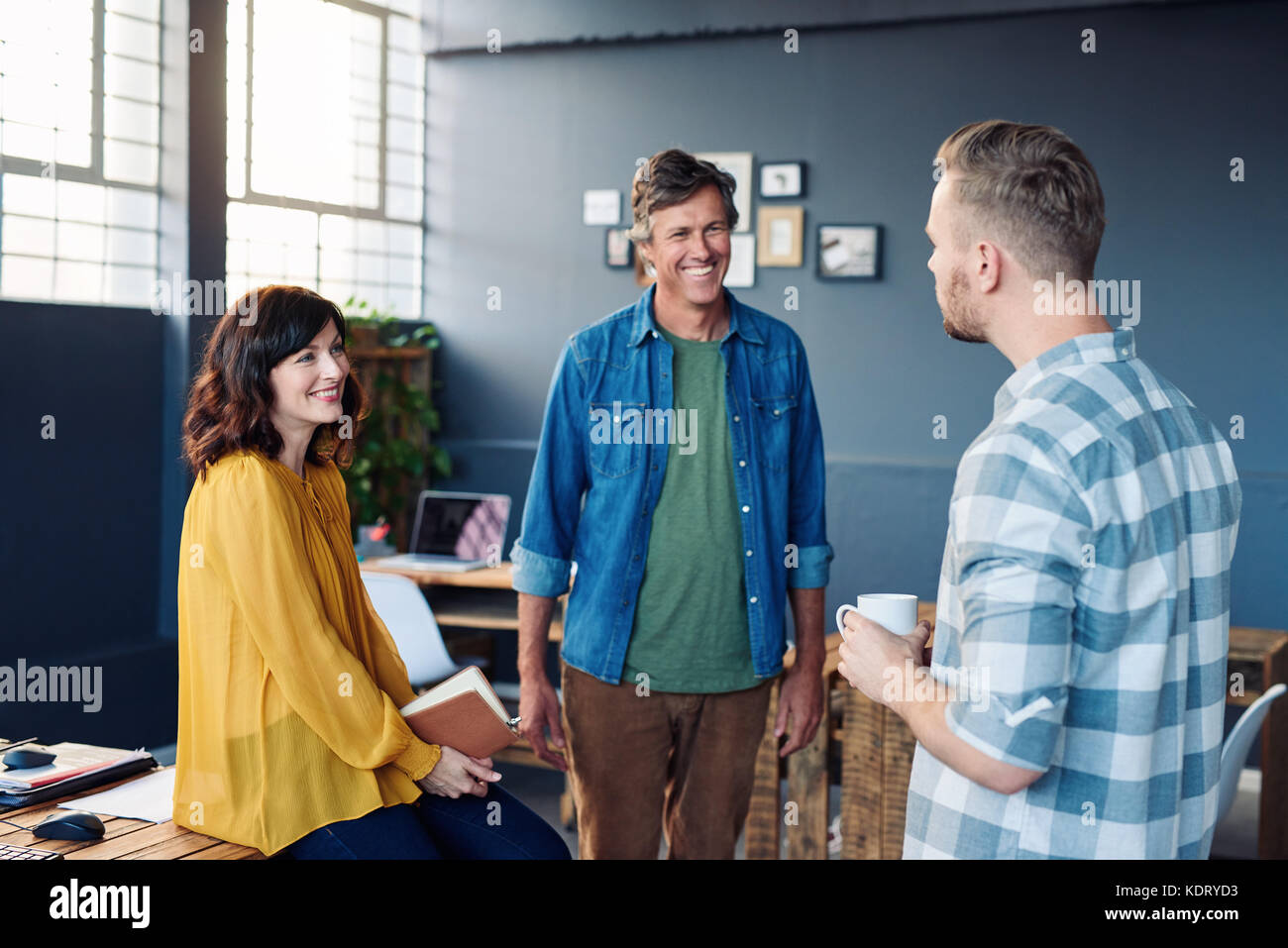 Three coworkers smiling and talking together in a modern office Stock Photo