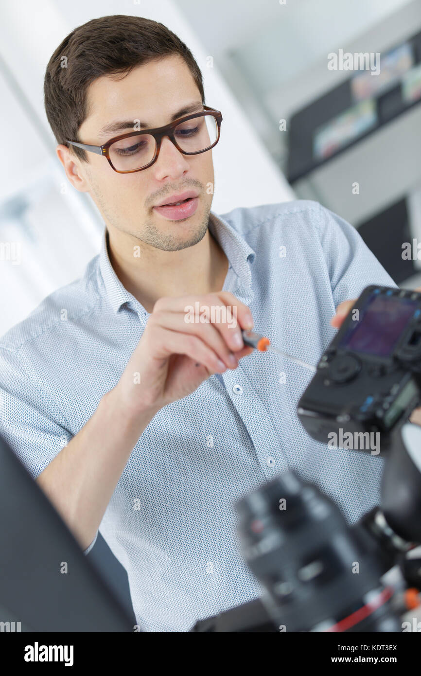 young confident technician is fixing and cleaning a digital cameralense Stock Photo