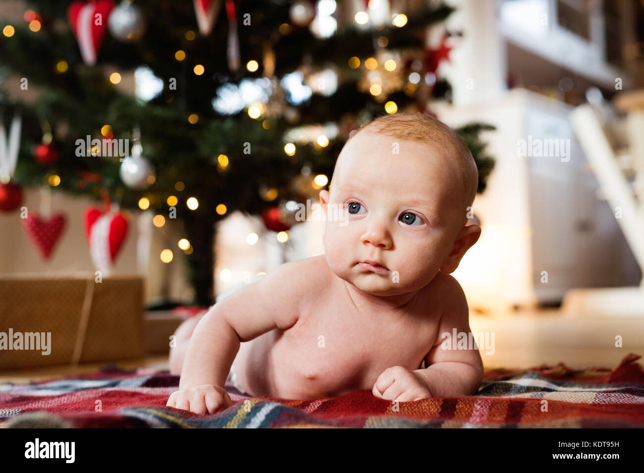 Cute little baby boy under Christmas tree lying on checked blanket
