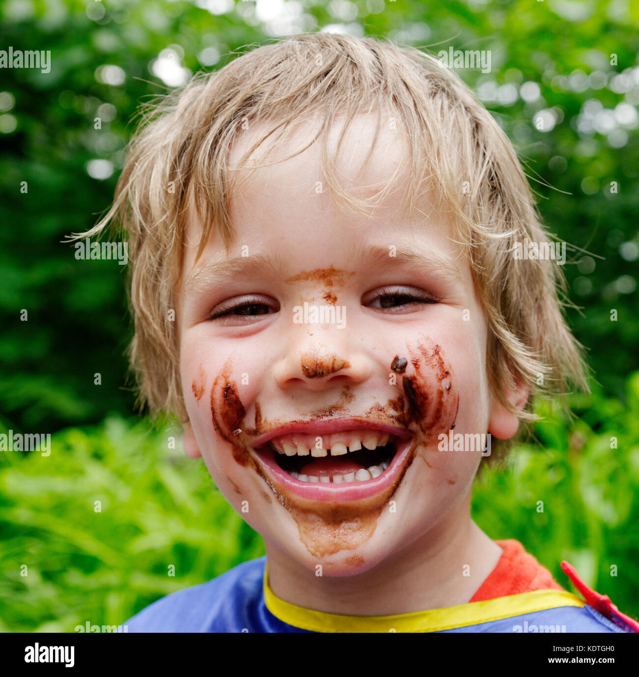 A little boy (5 yrs old) laughing with his face covered in chocolate after eating a chocolate ice cream Stock Photo