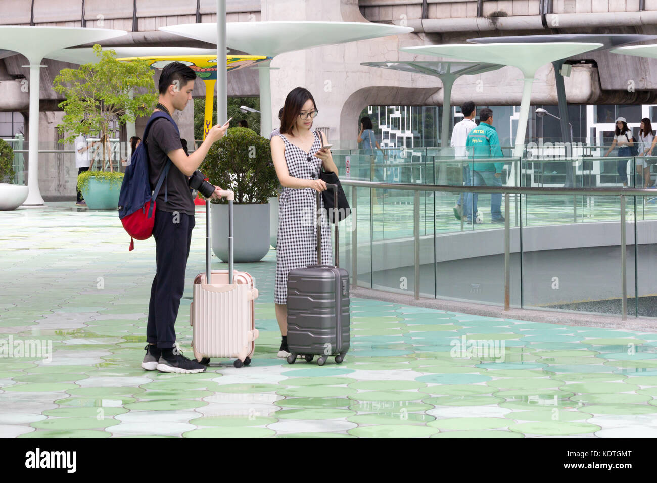 Asian couple with suitcases consulting their phones for directions, Bangkok, Thailand Stock Photo
