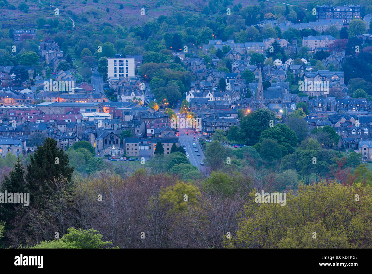 Evening view of Ilkley town centre nestling in Wharfe Valley - residential buildings, high street, lights on & moors - West Yorkshire, England, UK. Stock Photo
