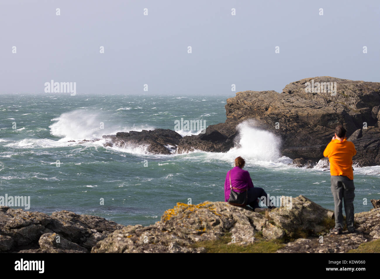 Anglesey, Wales. 16th Oct, 2017. UK Weather.  As forecasted with Yellow and Amber and the more dangerous Red warnings by the Met Office Hurricane Ophelia will begins to make landfall to most western parts of the UK including Wales bring storm weather and sea surges as this couple discovered photographing the waves dangerously close to the sea edge at Treaddur Bay, Anglesey Stock Photo
