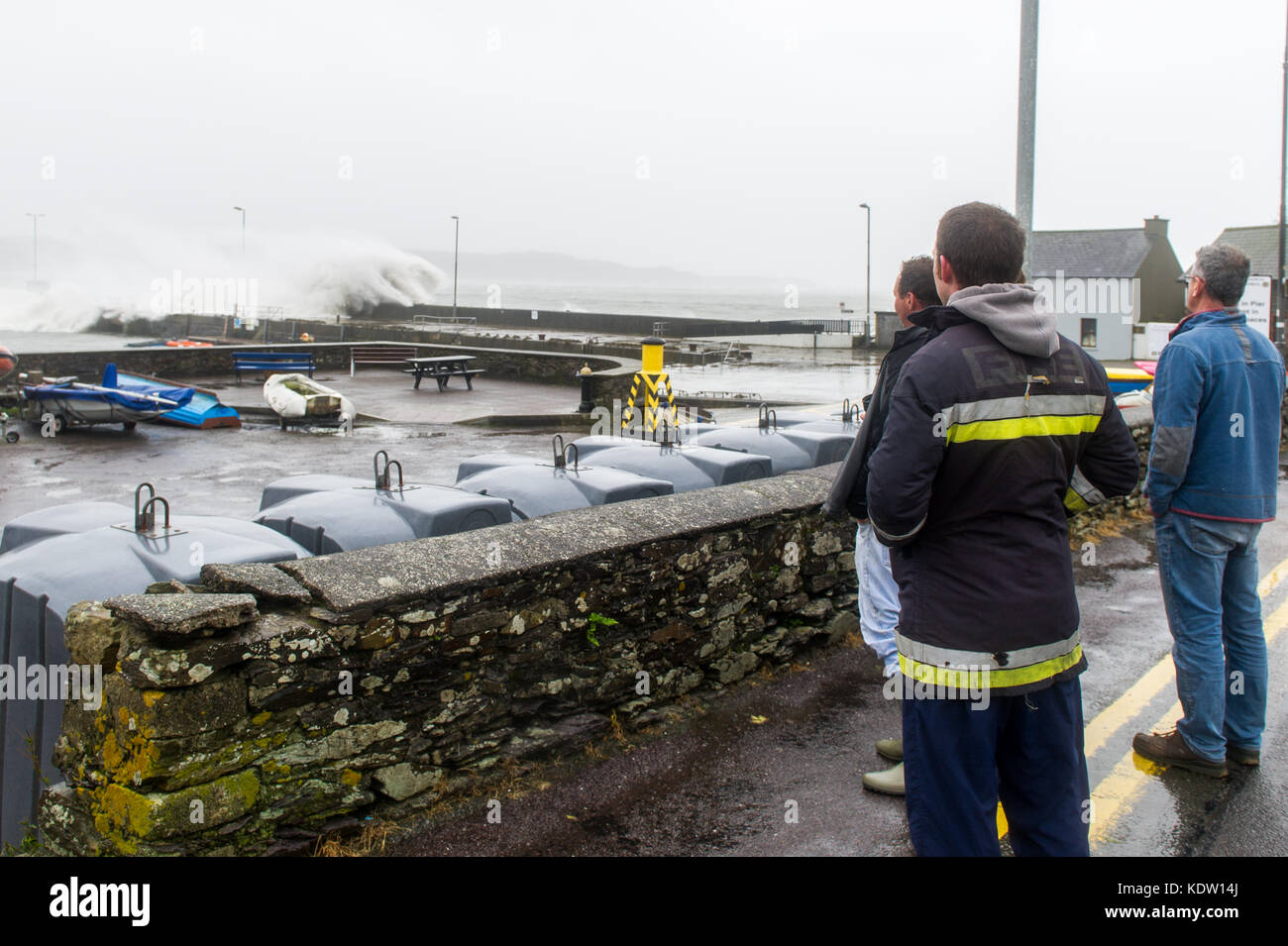 Schull, Ireland 16th Oct, 2017.  Ex-Hurricane Ophelia hits Schull, Ireland with winds of 80kmh and gusts of 130kmh.  Major structural damage is expected as the worst is yet to come. A group of local fishermen watch the waves crash over Schull pier. Credit: Andy Gibson/Alamy Live News. Stock Photo