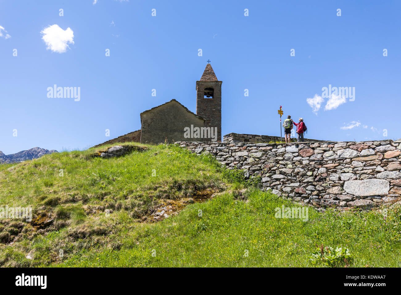 Hikers at the ancient church of San Romerio Alp, Brusio, Canton of Graubünden, Poschiavo valley, Switzerland Stock Photo