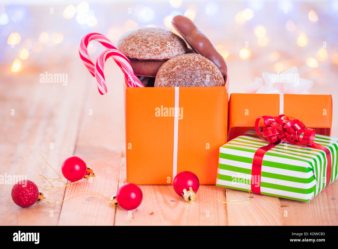 Presents with gingerbread and candies inside, on a wooden table, surrounded by red globes and blurred Xmas lights in the background. Stock Photo