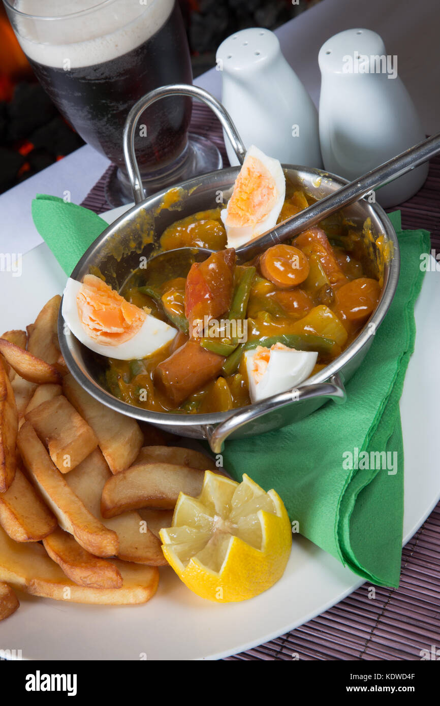 English pub meal of Curried Sausage with boiled egg and potato chips/fries with a glass of ale/beer Stock Photo