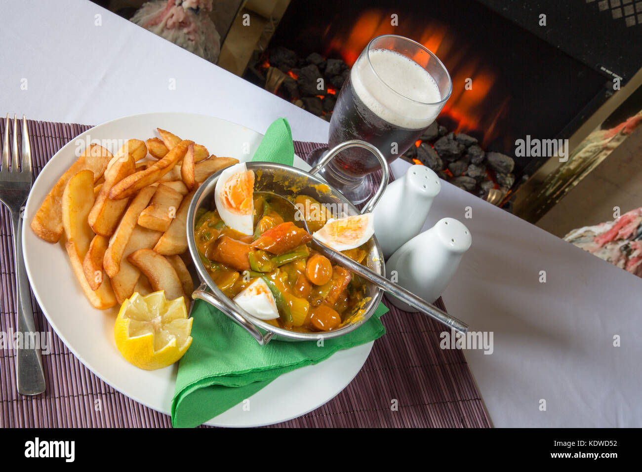 English pub meal of Curried Sausage with boiled egg and potato chips/fries with a glass of ale/beer Stock Photo
