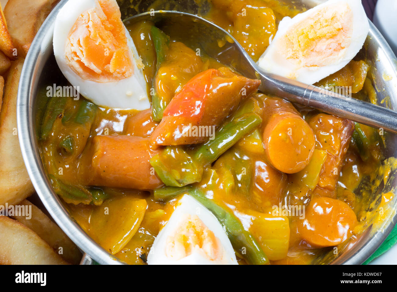 English pub meal of Curried Sausage with boiled egg served in a kahari bowl and a side of potato chips/fries Stock Photo