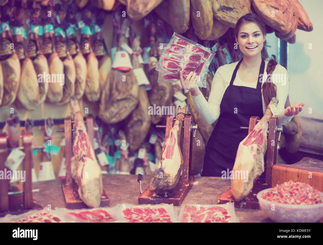 happy spanish female butcher with lard and meat in counter of store