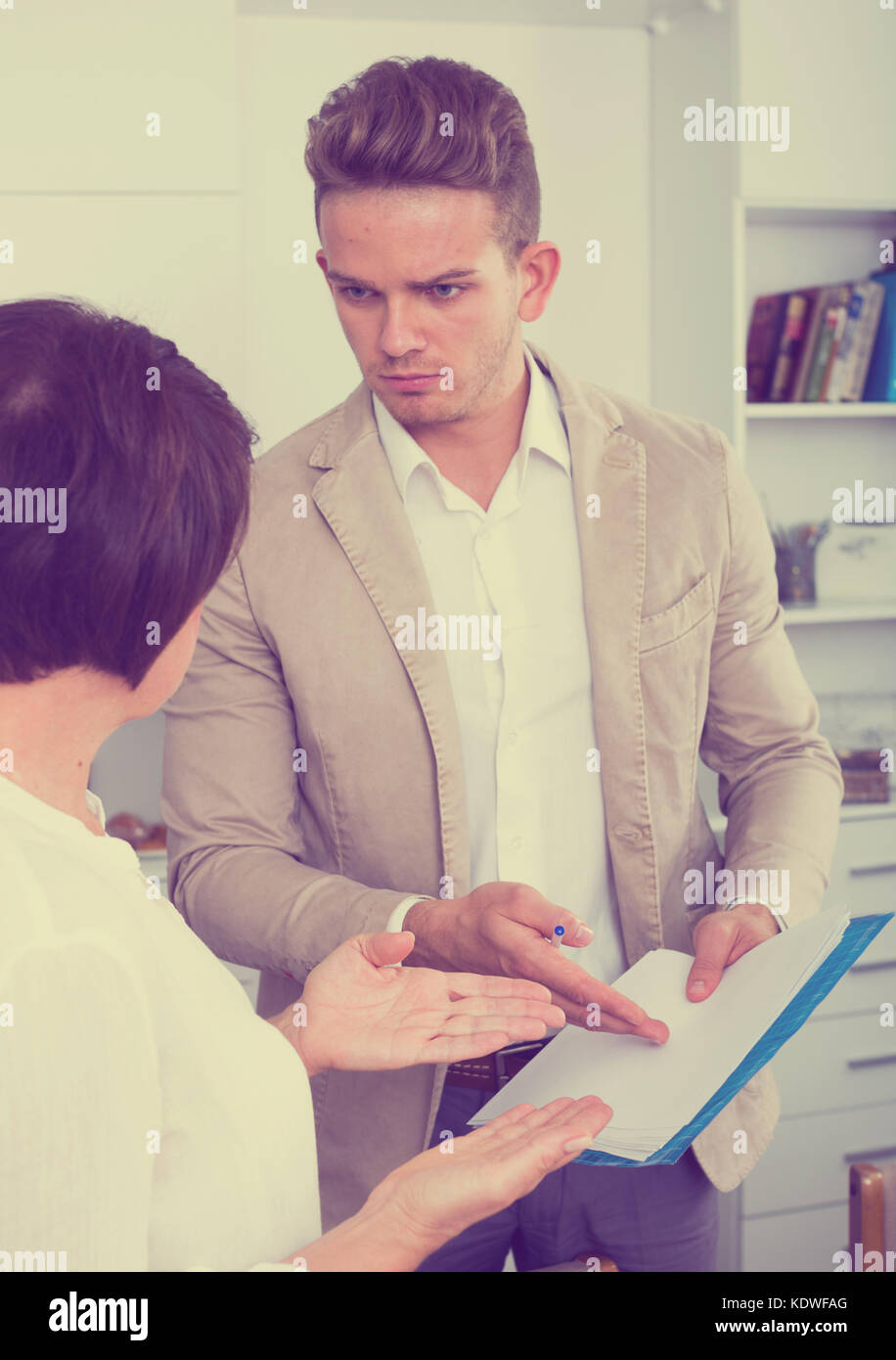 Young man tries to persuade elderly woman to sign documents Stock Photo