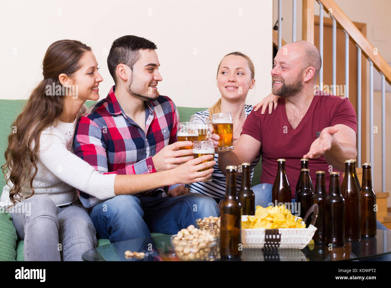 Positive friends hanging out with beer and snacks in home Stock Photo ...