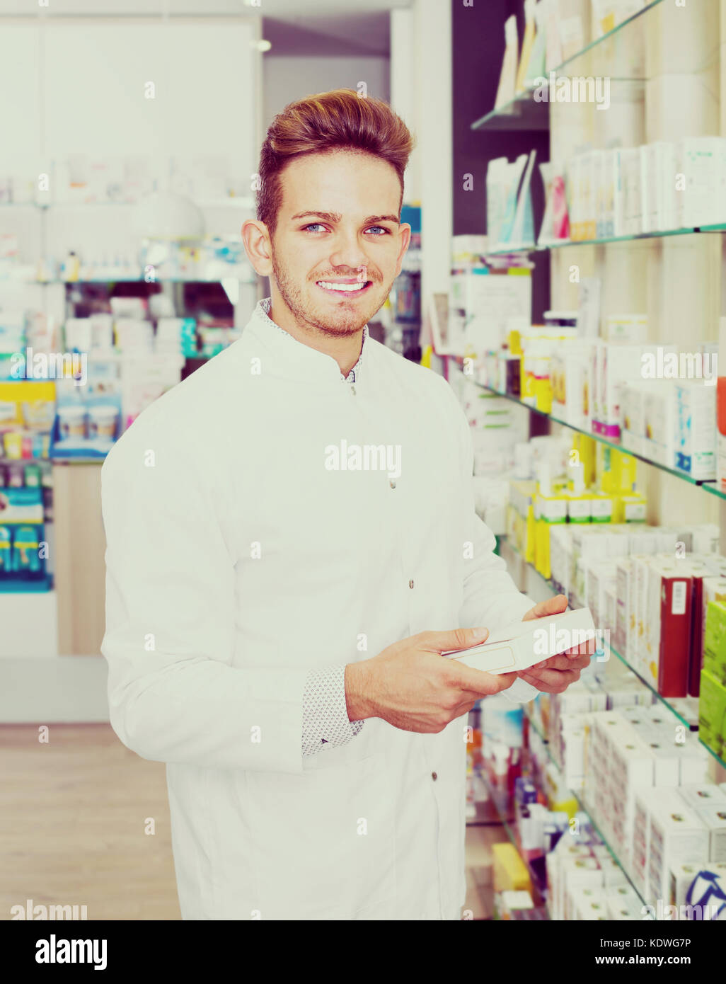 Smiling positive male pharmacist wearing white coat standing among ...