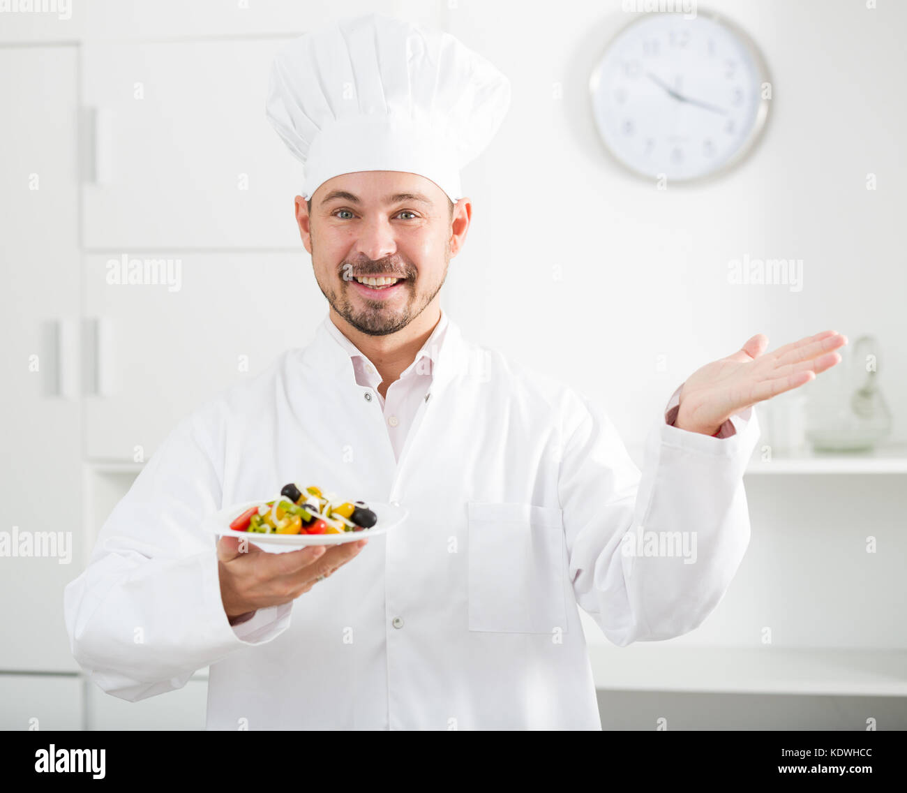 European Cook Young happy european cook in cap offering greek salad for lunch Stock ...