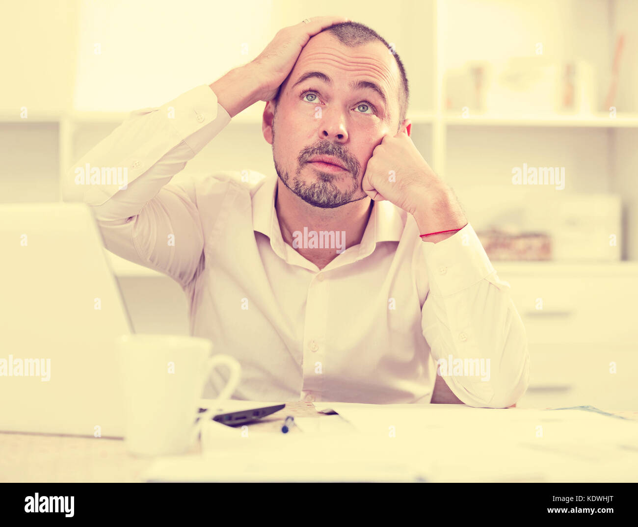 Disappointed worker at his office table feeling stressed, thinking and looking up Stock Photo