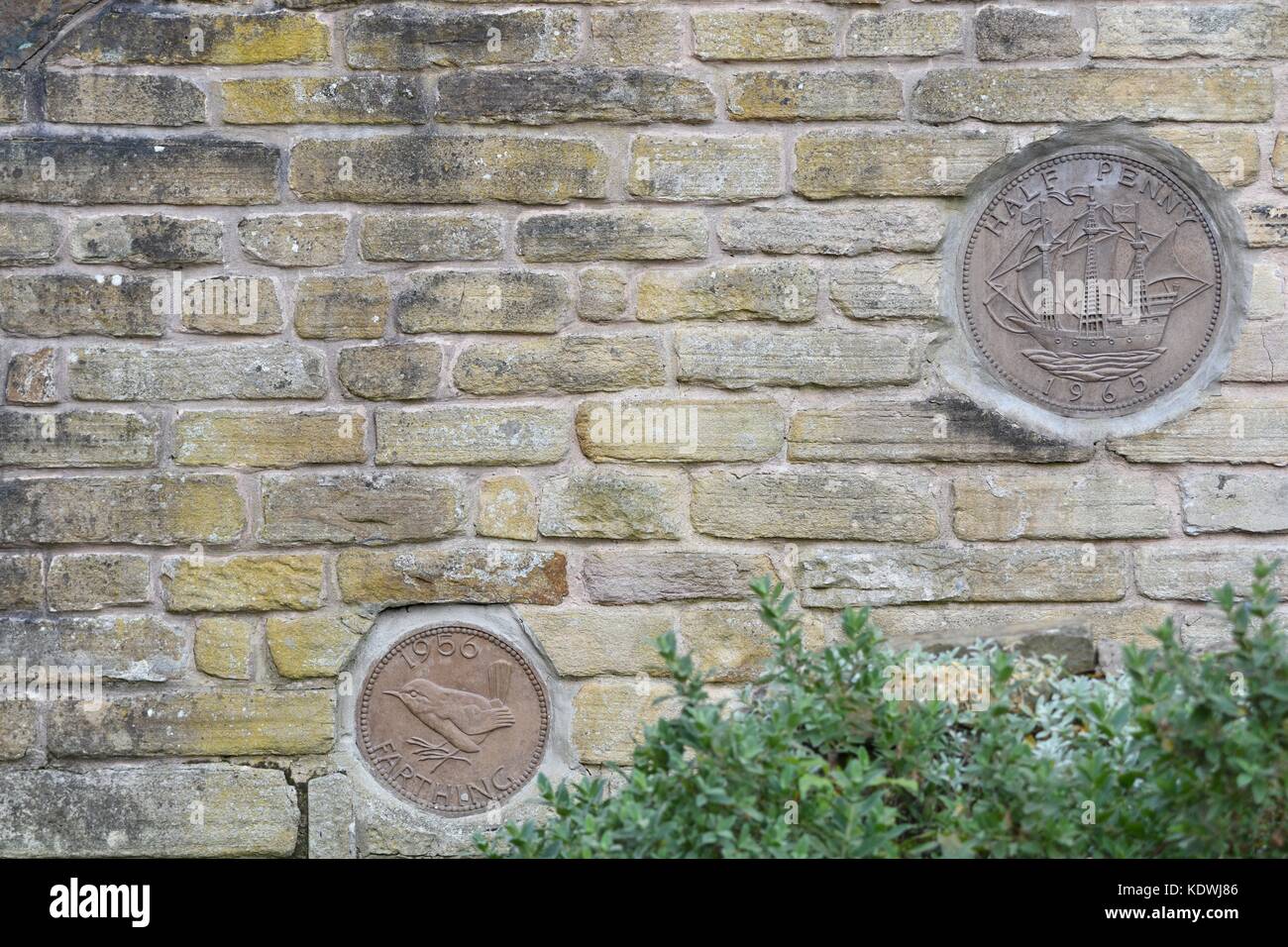 A giant farthing and half-penny are built into a wall of a house in New Mills, Derbyshire Stock Photo