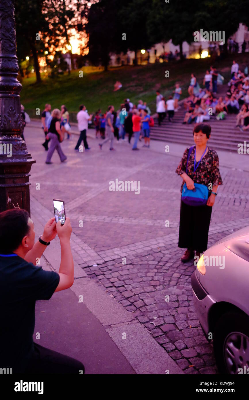 A husband takes a photo of his wife in Montmartre, Paris at the steps of Sacre Couer, using his smartphone Stock Photo