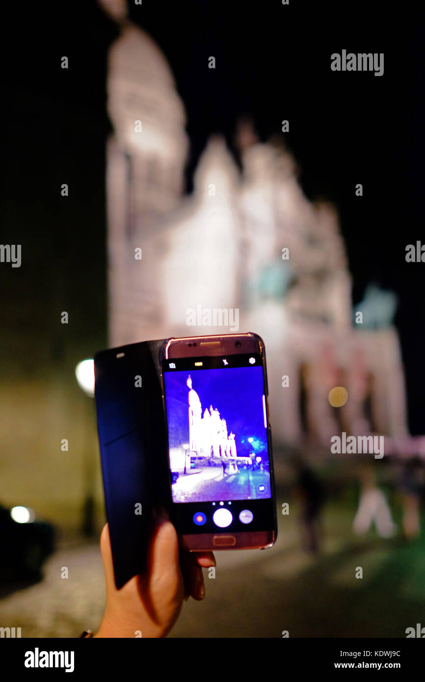 A tourist taking a photo on her Samsung smartphone of Sacre Couer in Motmartre, Paris at night Stock Photo