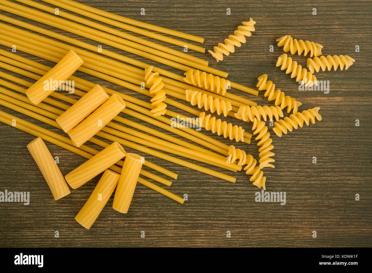 Selection of Raw Uncooked Italian Style Pasta Spaghetti Rigatoni and Fusilli With Copy Space On A Green Wooden Background Stock Photo