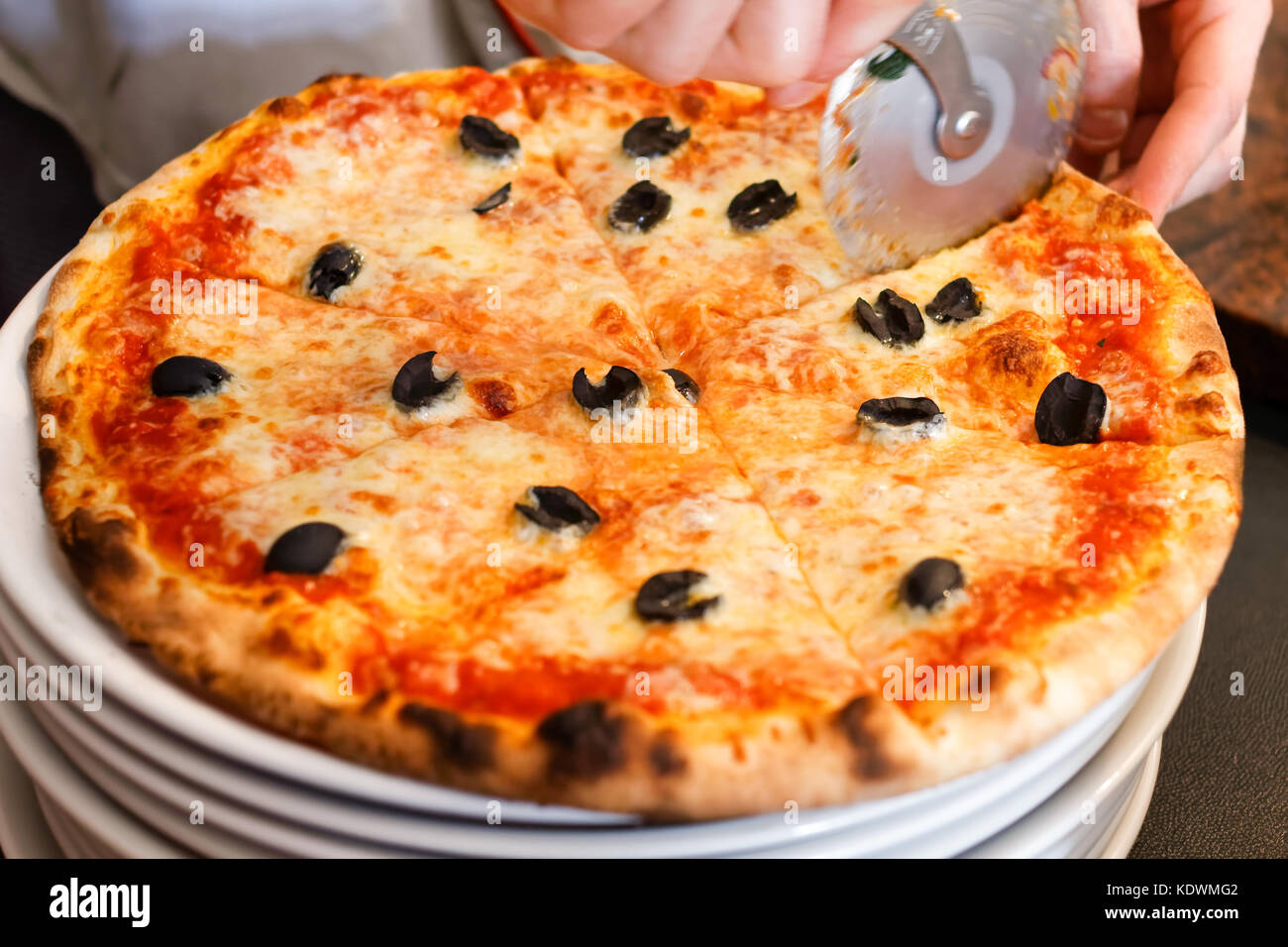 Cutting cheese pizza with pizza slicer. Stock Photo