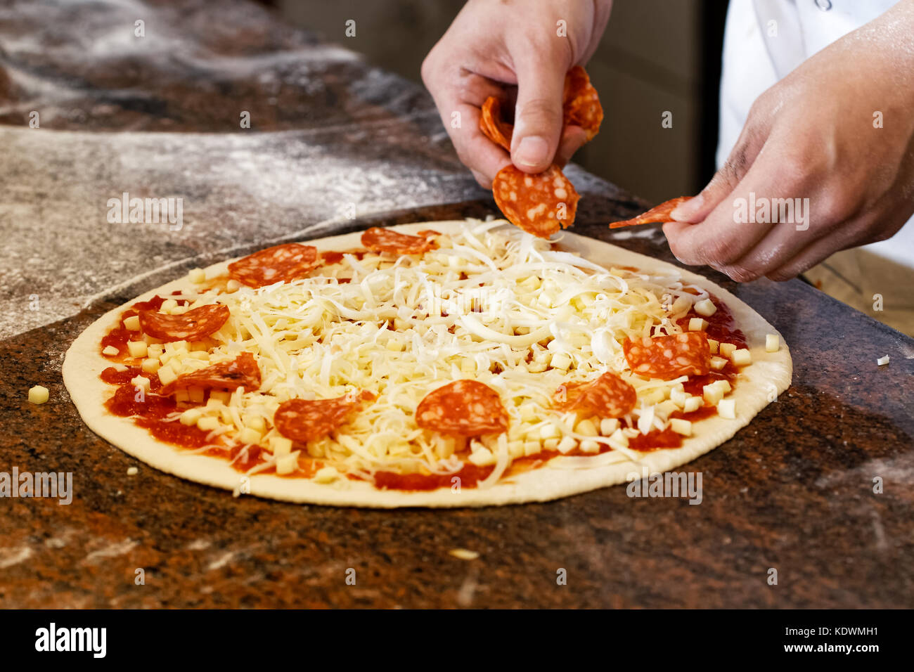 Cook's hands putting salami on tomato base pizza Stock Photo Alamy