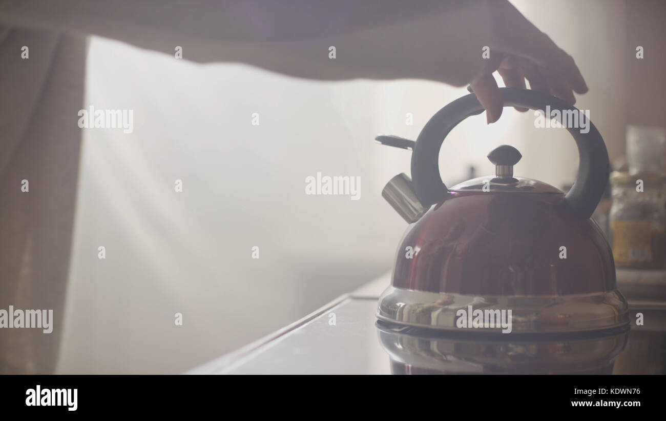 Girl put blue kettle on a kitchen gas stove. Stovetop whistling kettle