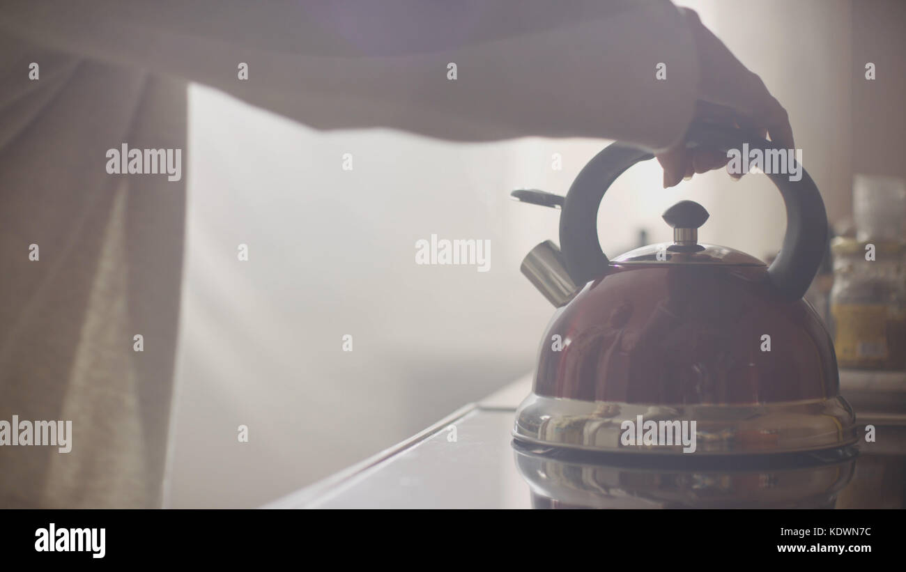 Girl put blue kettle on a kitchen gas stove. Stovetop whistling kettle