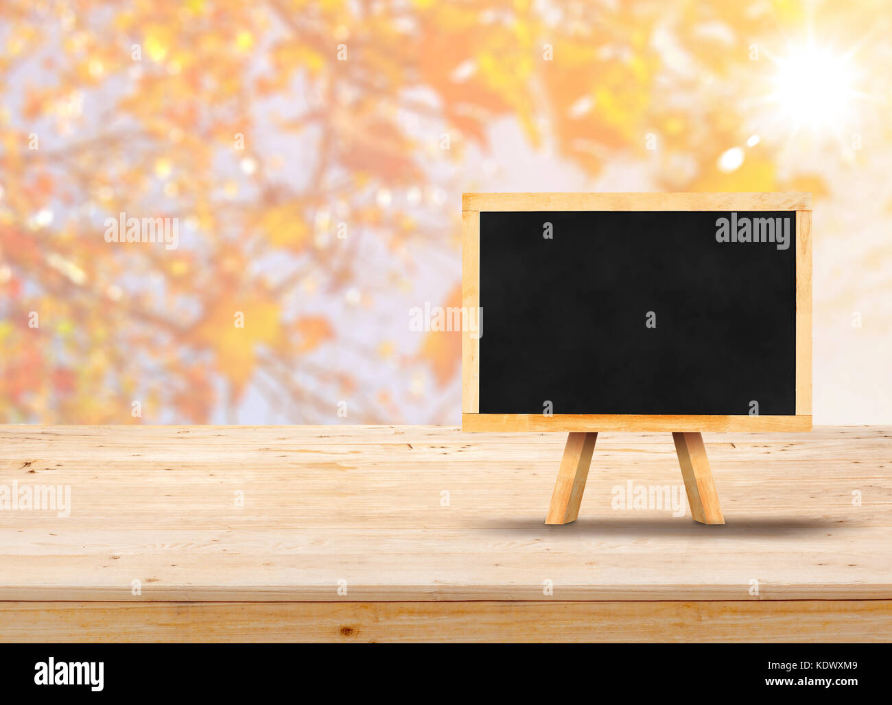 Blackboard with easel on wood table top with blur maple leaf with sunlight,Autumn backgorund,Mock up for display or montage of product,banner for adve Stock Photo