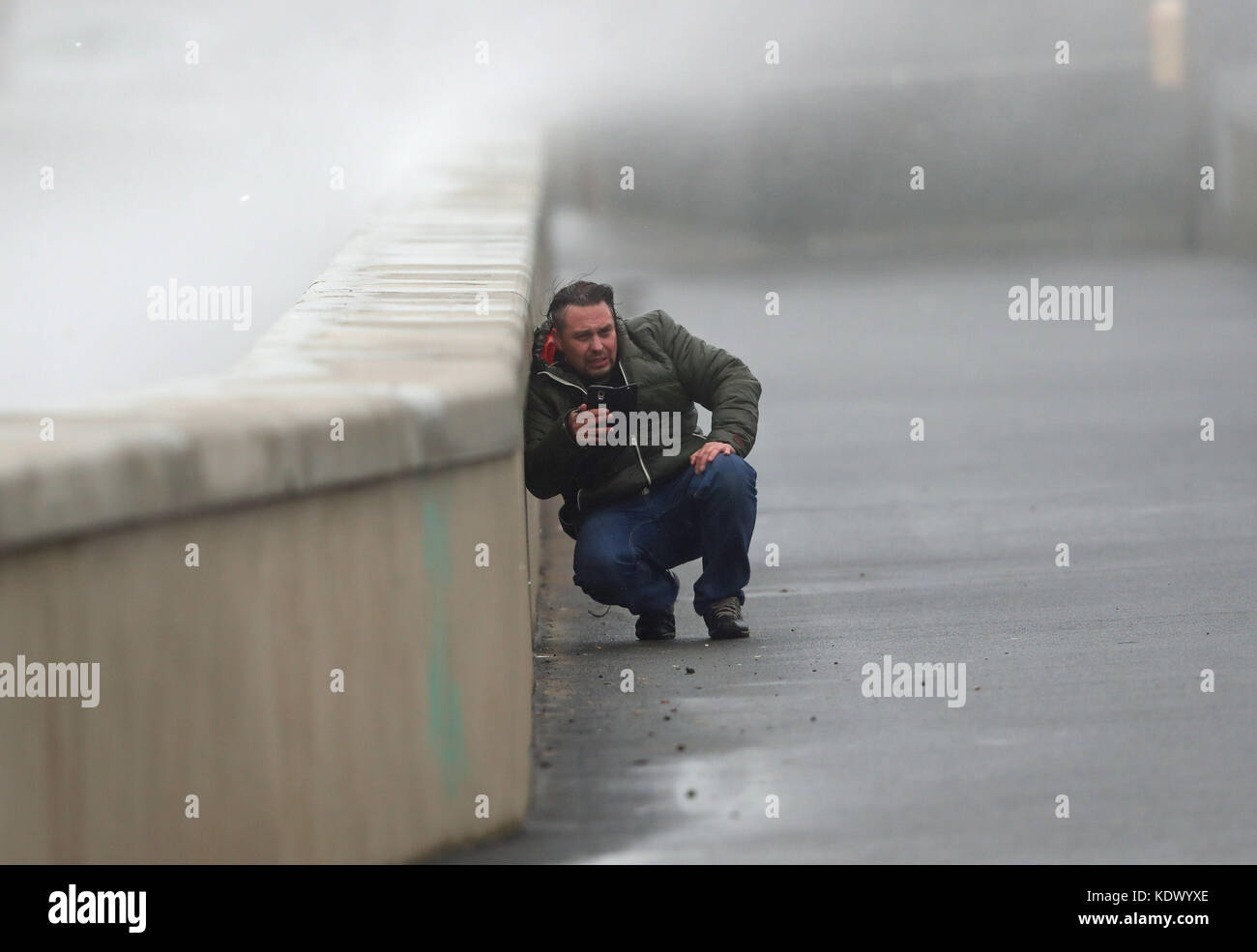 A man shelters from the waves and high wind at Lahinch in County Clare on the West Coast of Ireland as Hurricane Ophelia hits the UK and Ireland with gusts of up to 80mph. Stock Photo
