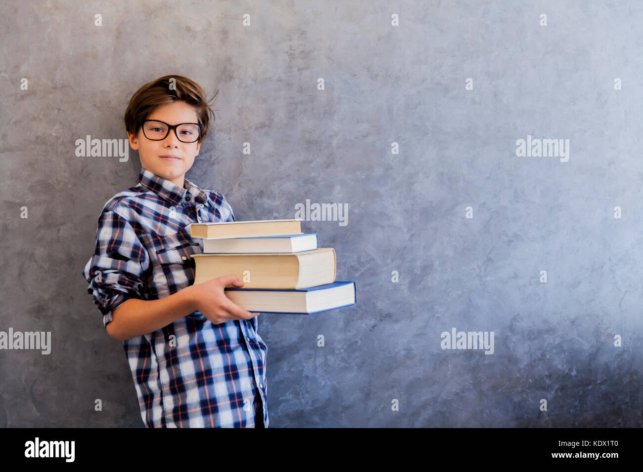 Cute teenage school boy holding books against wall Stock Photo - Alamy