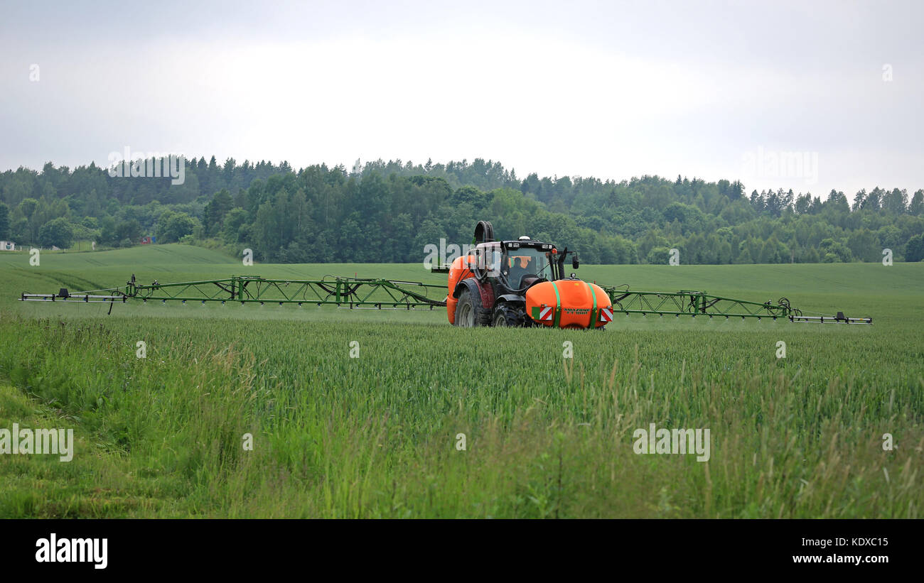 SALO, FINLAND - JUNE 25, 2016: Farmer sprays wheat field with Valtra tractor and Amazone 1501 UF mounted sprayer in June in South of Finland.  The boo Stock Photo