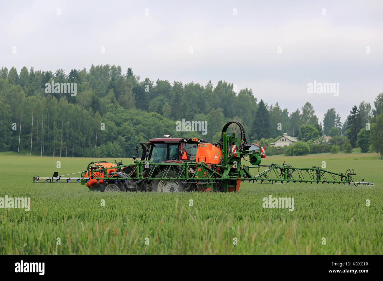 SALO, FINLAND - JUNE 25, 2016: Farmer sprays wheat field with Valtra tractor and Amazone 1501 UF mounted sprayer in June in South of Finland. Stock Photo