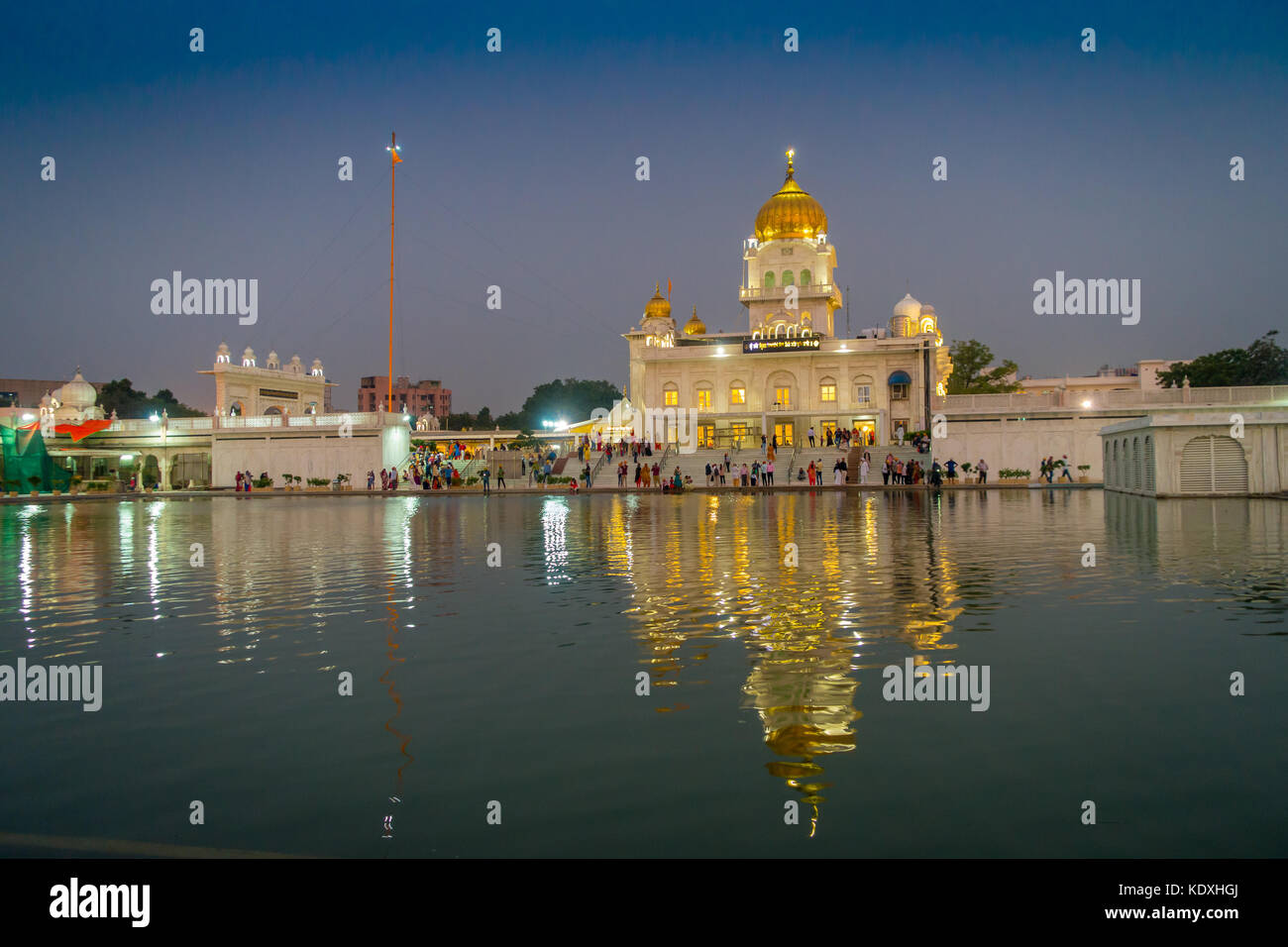 DELHI, INDIA - SEPTEMBER 19, 2017: Unidentified people walking in front of the main Sikh shrines of Delhi - Gurudwara Bangla Sahib. The main building of the temple is illuminated and is reflected in Sarowar pond water in India. Stock Photo