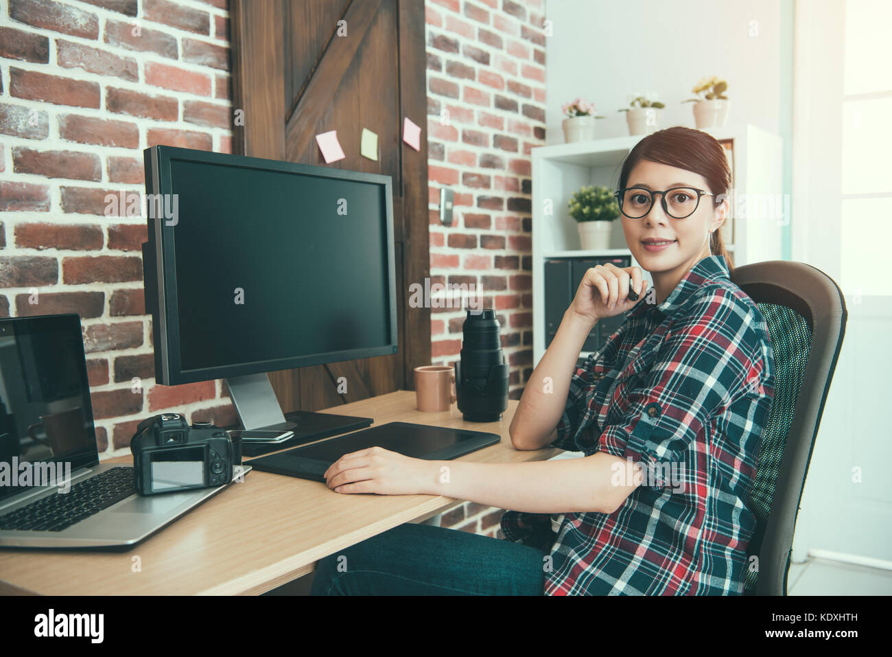 smiling confident woman right office worker designer sitting in working desk editing retouch photographer picture and looking at camera smiling. Stock Photo