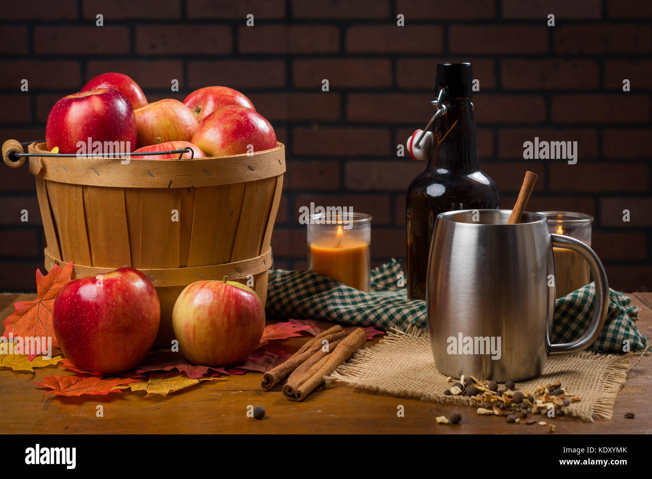 Silver mug with a cinnamon stick next to basket of apples Stock Photo