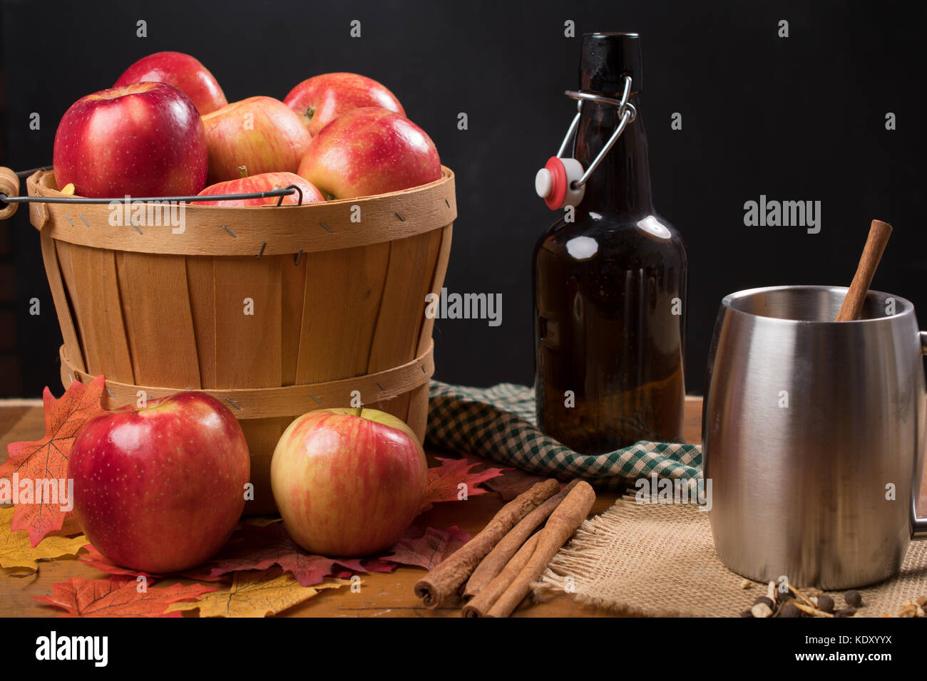Apple cider in a silver cup next to basket of apples in rustic setting Stock Photo
